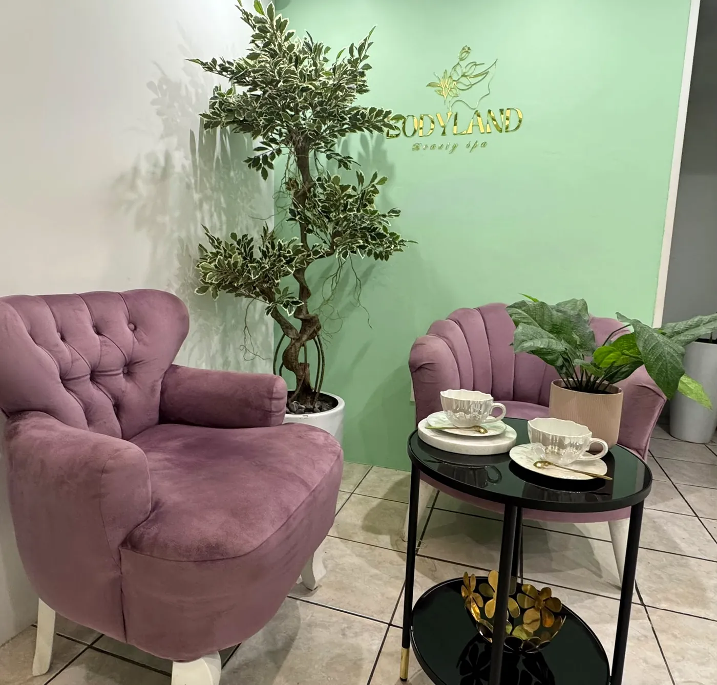 Recepción de Bodyland con sillones de terciopelo, tazas de té y el logotipo dorado en la pared